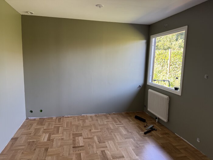 Rum med nylagt ekgolv, mösterpassat, grönmålade väggar, fönster med utsikt, och några verktyg kvar på golvet.