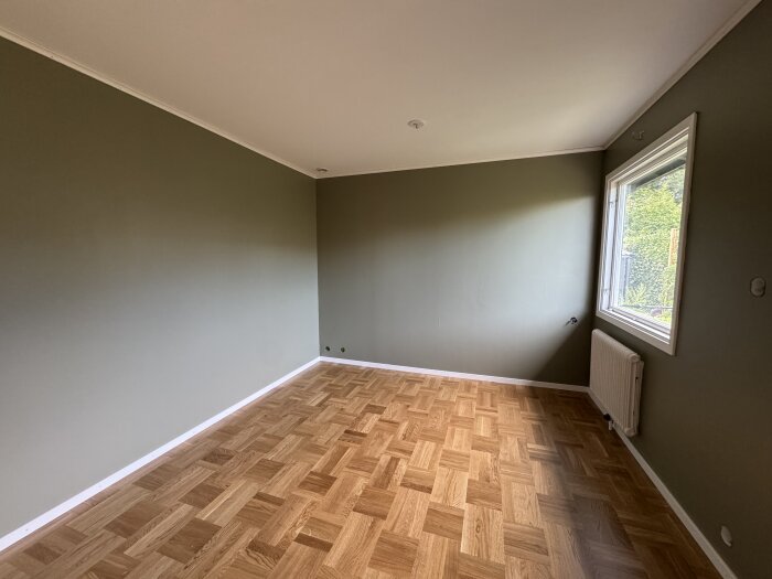 Rum med nylagt fiskbensmönstrat parkettgolv i ek, målade gröna väggar och ett stort fönster, sett en solig dag.