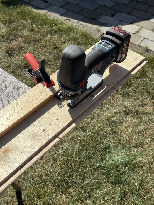 Sticksåg och träbräda utrustade med en tving, placerade utomhus på en gräsmatta.