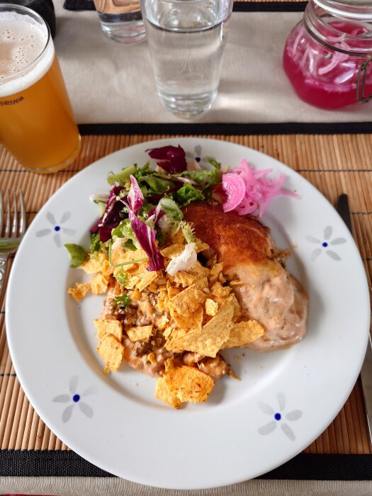 En tallrik med enchiladas, köttfärs, Creme Fraiche, tacosås, sallad och picklad rödlök, serverad med ett glas öl och vatten.