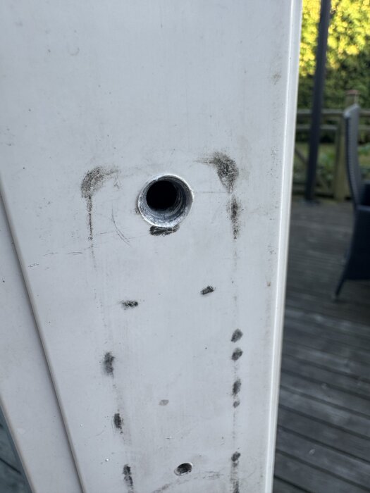 Hål i en vit dörrkarm med smuts runt, förberedelse för montering av handtag med blindnitsmutter, visar borrning och materialskikt.