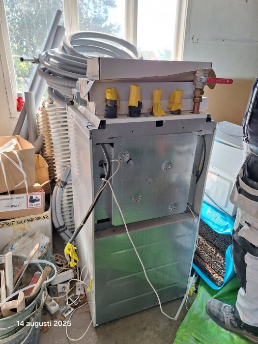 Värmepanna med anslutningar, omgiven av verktyg och material, i renoveringsmiljö. Inga synliga märken eller modeller.