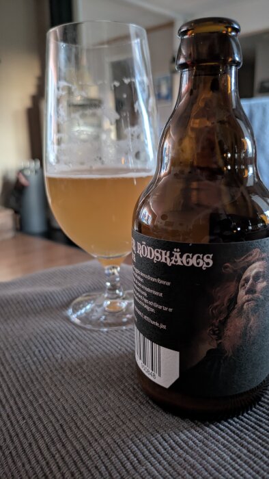 Flaska med öl och ett glas med Fader Rödskäggs Ipa från Vreta Kloster står på ett bord.