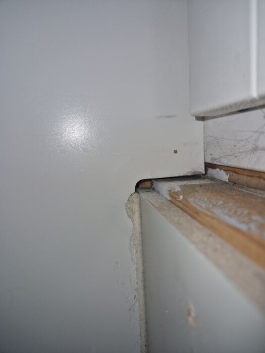 Springa under fönsterbräda med trä- och masonitskiva, synliga reglar och isolering i bakgrunden. Möjlig ventilationsöppning eller felbygge.