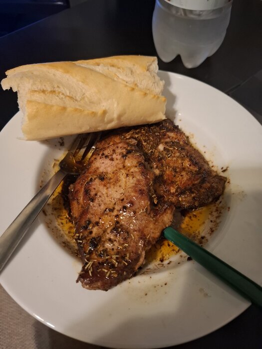Fläskkarré med kryddor och smör på en tallrik, serverad med en baguette och en flaska vatten i bakgrunden.