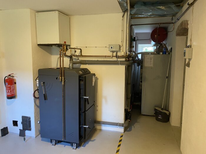 Vedpanna RB Ventum i tvättstuga, rör och expanderingskärl synliga. Brandsläckare på väggen bredvid.