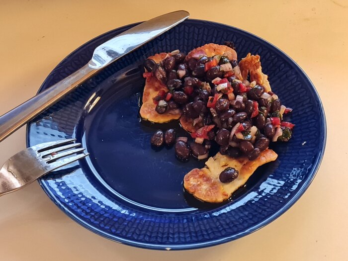 Stekt halloumi med bönröra på en blå tallrik, serveras med kniv och gaffel.