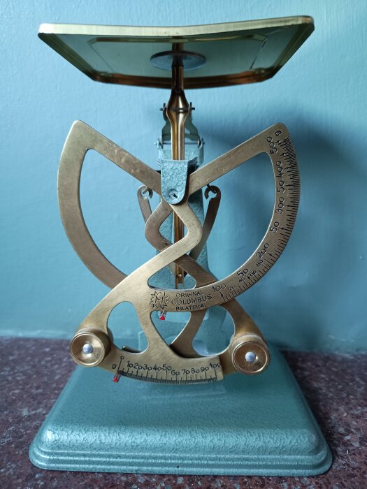 Äldre brevvåg med dubbla skalor, mäter upp till 500 gram, med en grön bas och guld-finish, mot en blå bakgrund.