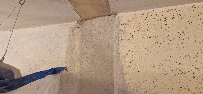 Närbild av hörn i tvättstuga med olika väggytor; en obränd putsad yta, del med sprickor och fläckar, samt ogenomtränglig färgad yta.