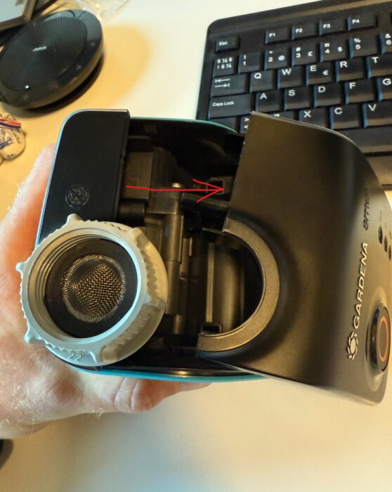 Gardena-enhet demonteras, instruktion med pil visar var clips och sladdfäste finns, tangentbord i bakgrunden.