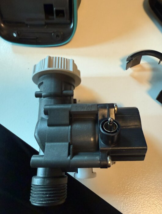 Ventil med clips för Gardena-enhet, liggande på ett bord, med en borttagen sladd och andra smådelar i närheten.