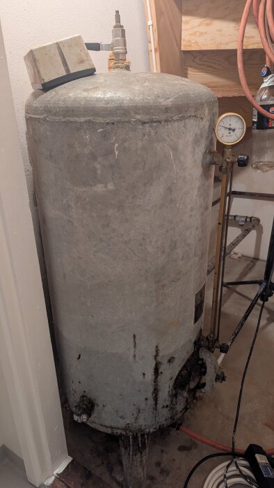 Äldre galvaniserad hydrofortank med tryckmätare och kopplingar, synlig rost vid basen. Används i en vattenanläggning från 1967.