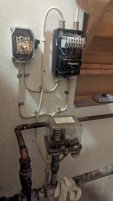 Äldre hydroforinstallation med exponerade elkablar, tryckströmbrytare och rörkopplingar i ett hem.