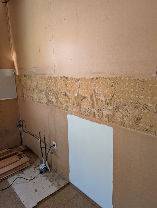 Vägg i kök med borttaget kakel; synligt gammalt kakellim och rör för diskho.