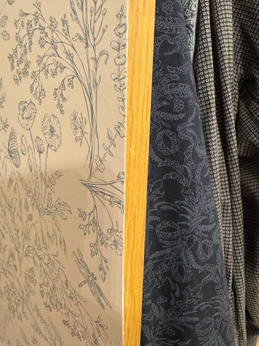 Garderobskant med blommig tapet och träram, intill klädhängare med mörkblå mönstrat tyg.