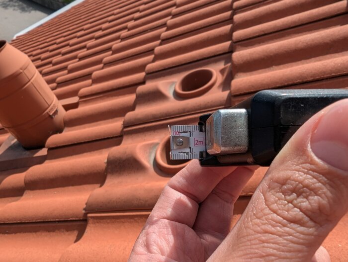 Mätband mot hål på tak med tegelpannor, visar cirka 113mm i diameter.