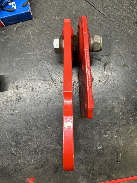 Röd metalldel med bult och mutter, redo för montering. Utbytesdel för reservmaskin efter reparation av slitet midjelager.