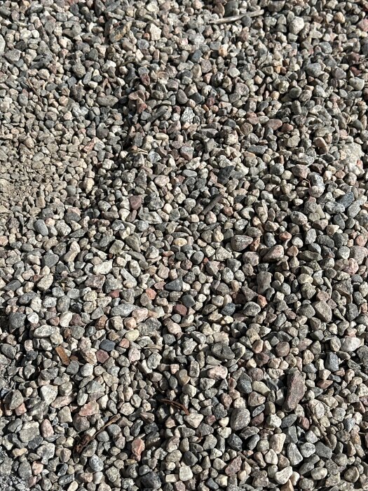 Närbild på gårdsgrus med små, ojämna stenar i olika färger.