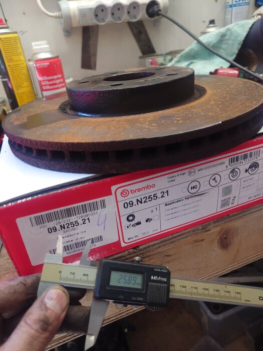 Rostig bromsskiva placerad på en röd Brembo-låda, med ett digitalt skjutmått som visar 25,89 mm tjocklek.