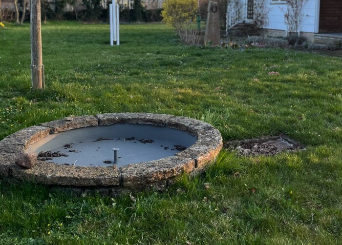 Gammal, rund fontän av murad kalksten och betong på en gräsmatta, med ett litet metallutlopp.