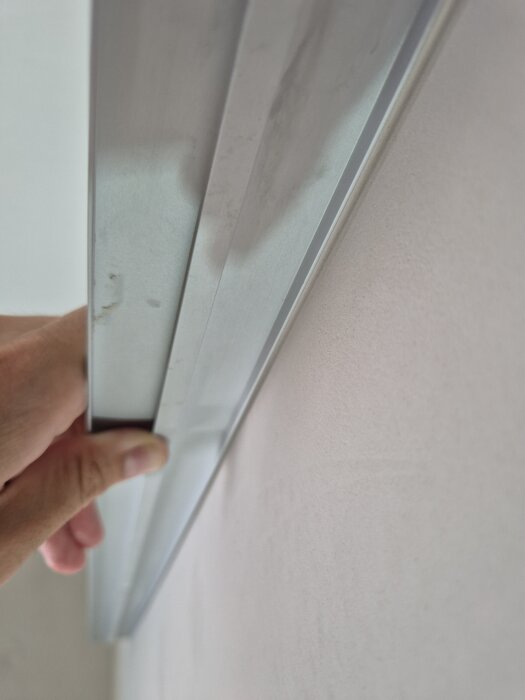 Person håller en tapetlinjal mot en spacklad vägg för att kontrollera ojämnheter i ytan.