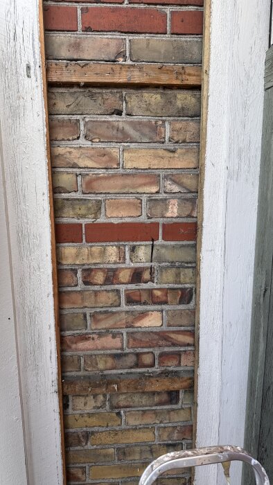 Ursprunglig tegelvägg delvis avtäckt, med olika färger på teglet och träreglar.