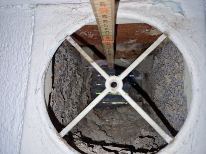 Närbild av en öppen ventilationsöppning med gamla inre ytor, måttband och korsram inuti, förberedd för installation av ny ventil.