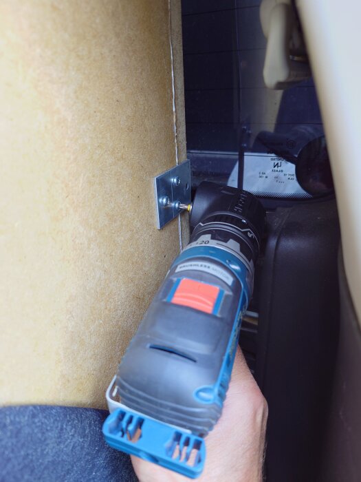 En person använder en vinkelchuck och borr för att montera ett vinkeljärn på insidan av en bilbaslåda.