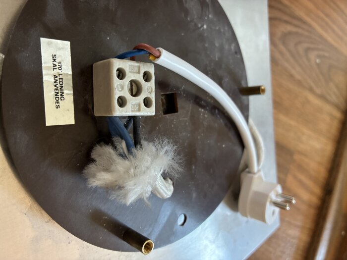 Ojordat taklampskoppling med dubbel blå och svart kabel anslutna till sockerbit. Jordad stickpropp där jordkabeln är klippt, på olivgrön platta.