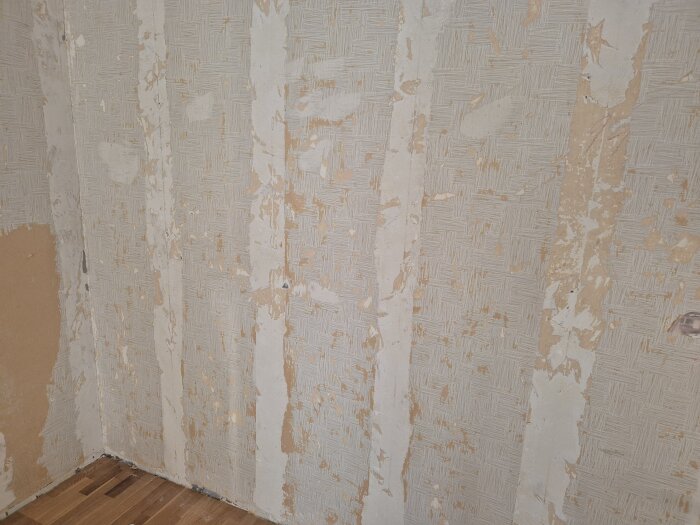 Vägg med gammal tapet och ojämnt spackel, tecken på försök att avlägsna tapet syns.