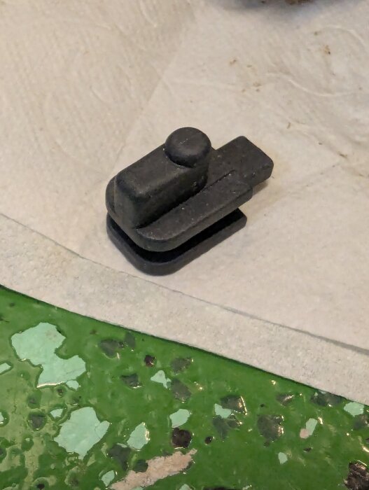 Svart metalldel på vit yta, del av mekaniskt projekt.