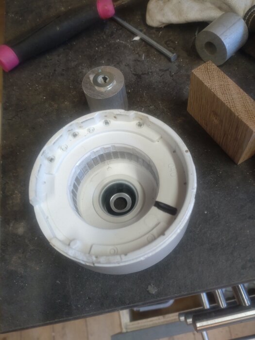 Del av luftvärmepumpens innerdel med nytt lager på arbetsbänk i snickarverkstad.