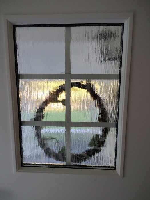 Sprucket glas i ytterdörr med ett dekorativt mönster synligt genom glaset, inomhusvy.