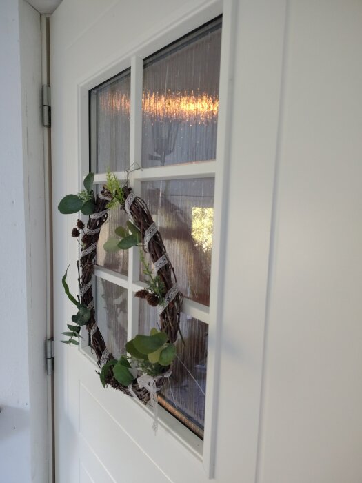 Ytterdörr med glasruta som har spruckit, dekorerad med en krans av grenar och gröna blad.