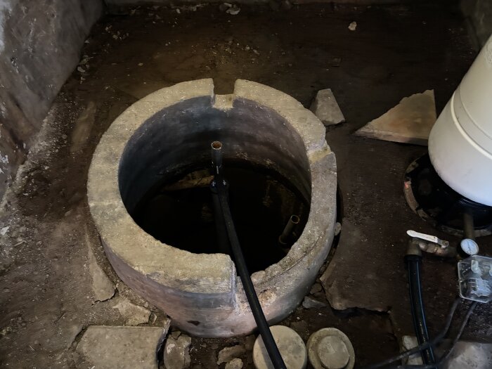 Vattenbrunn med trasig brunnsring inne i en jordkällare med rör och hydropress synliga.