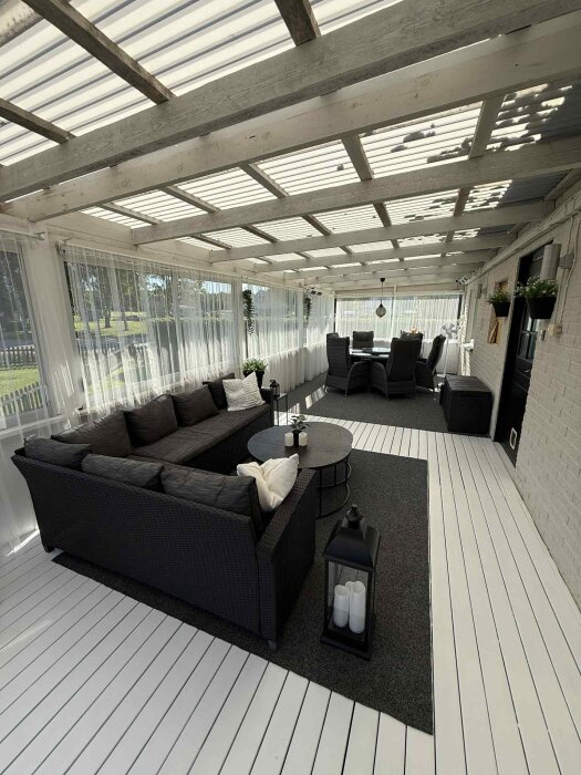 Möblerad altan med mörk soffa, runda bord, ljus träpanel, lykta med ljus och mysig atmosfär.