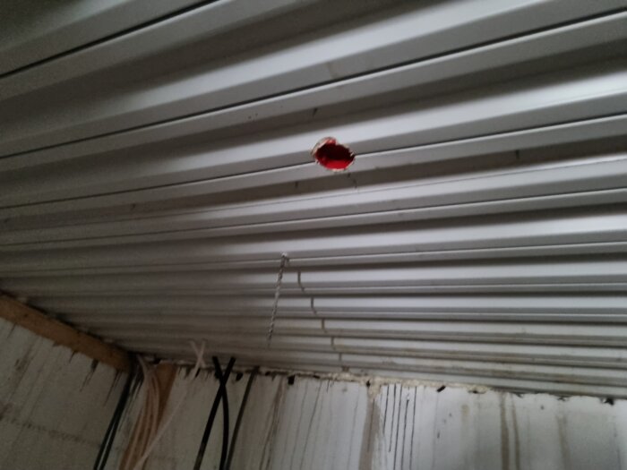 Hål borrat i taket på en källare med några synliga kablar och rör, eventuellt för att följa golvslingan från badrummet ovanför.