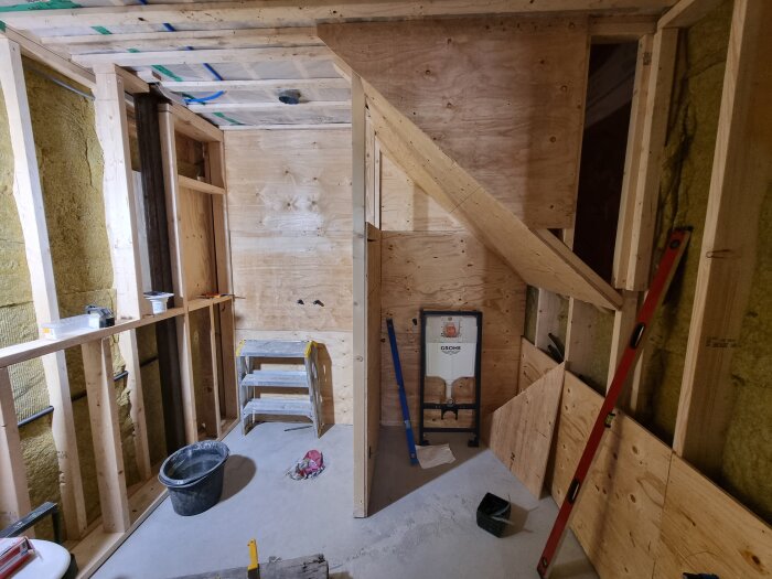Renovering av badrum under arbete med trästomme, nivåmätare, byggstege och material på plats.