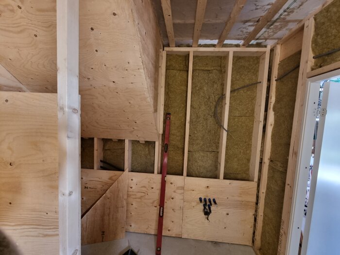 Renovering av badrum under konstruktion, med träpaneler och synliga isoleringsmaterial i väggarna; röda byggverktyg syns också.