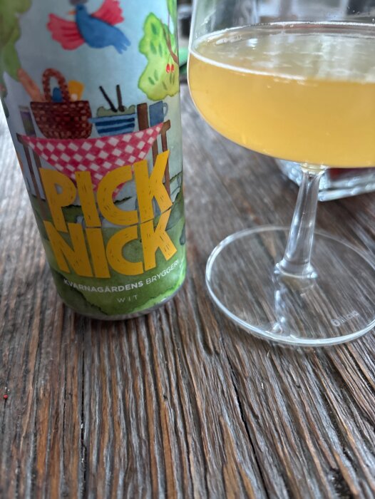 Burk med etiketten "Picknick" och texten "Kvarngårdens Bryggeri" bredvid ett glas med ljus öl på ett rustikt träbord.