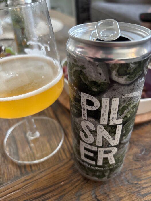 En halvtom glasflaska med öl bredvid en öppnad ölburk från Kvarngårdens bryggeri med texten "Pilsner" på etiketten.