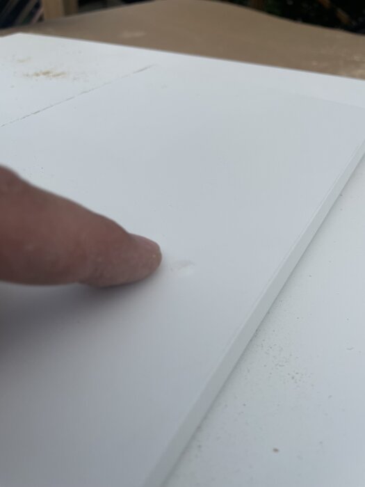 En finger pekar på ett borrhål i en vit IKEA-lucka som är 16 mm tjock, med borrspån runt omkring.