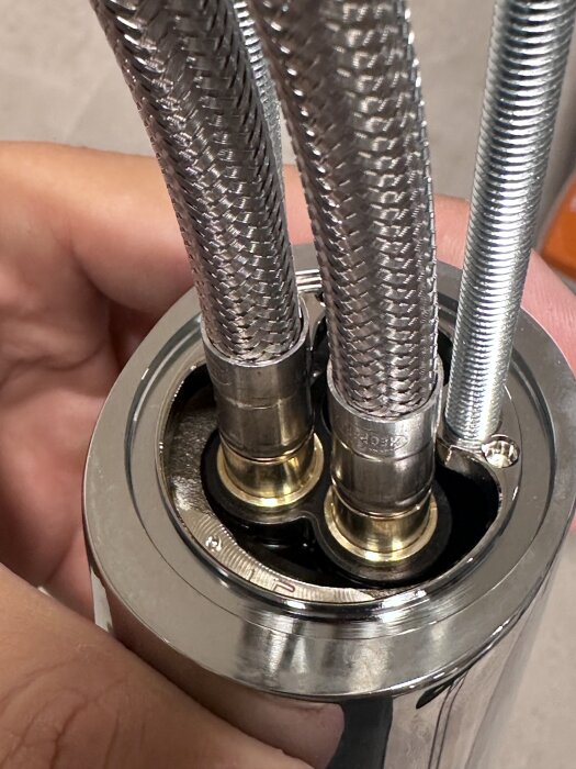 Flexibla metallslangar anslutna till en beslag i en vatteninstallation, hållna av en hand.