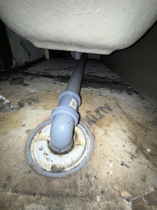 Avlopp under badkar med synlig fiberduk och mikrocementerad yta nära avloppet, där en lucka har tagits bort, renovering ca fyra år gammal.