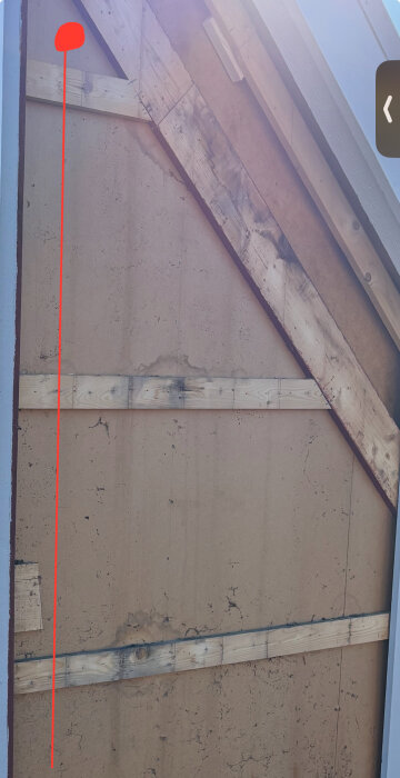 Vägg med träreglar och röd linje som visar kabeldragning utmed fasaden, börjar vid röd cirkel vid överkanten av väggen.
