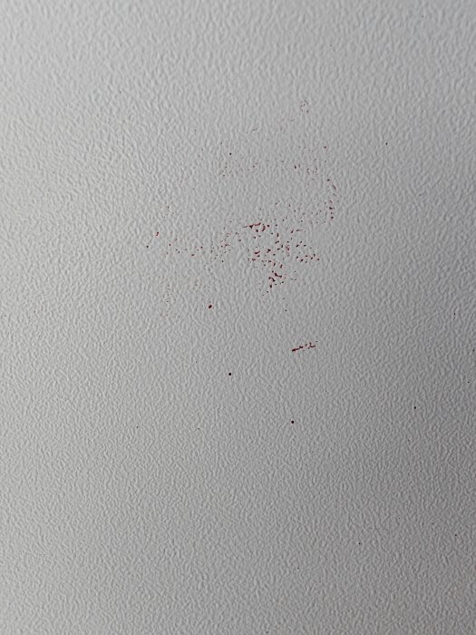 Texturerad yta på elskåp med röd färg fläckvis kladdad på, svårt att ta bort utan att skada ursprungsfärgen.