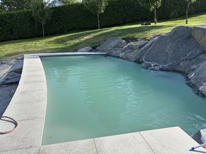 Betongpool inbyggd i berg med mjölkigt vatten och stenplattor runt, omgiven av grönska.