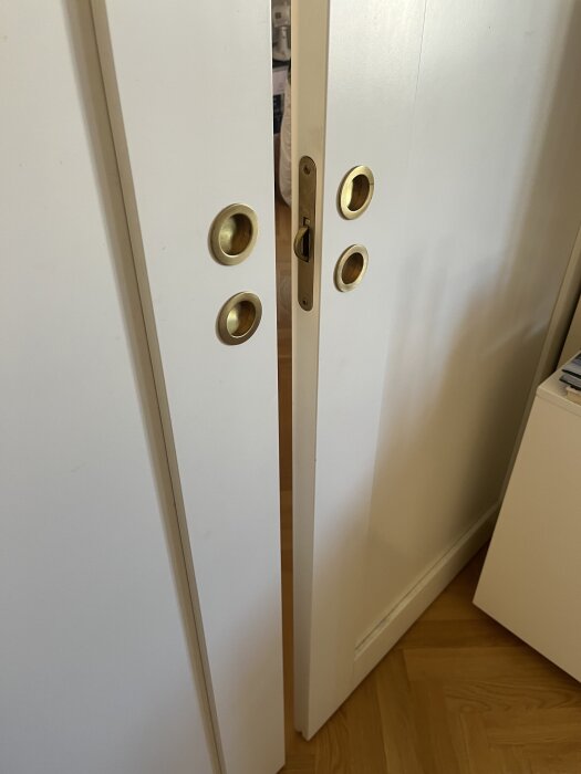 Vita skjutdörrar med mässingshandtag, synliga glipor mellan dörrar och golv, dålig ljudisolering i lägenhet mellan sovrum och vardagsrum.