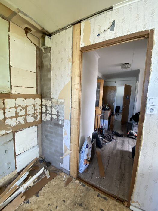 En borttagen dörrkarm visar ett träbjälke mot murstocken i ett rum under renovering, med verktyg och material på golvet.