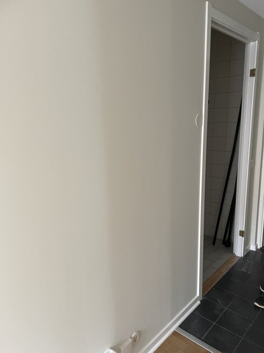Målade väggar med synliga ojämnheter bredvid en dörröppning och golv av olika material, indikerar bristande underarbete.
